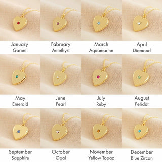 Gold heart-shaped birthstone necklaces on a beige fabric background