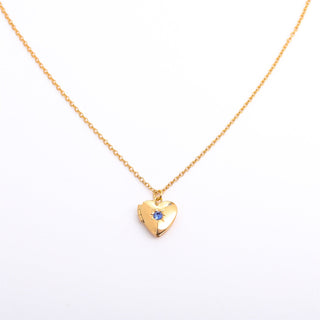 Gold heart-shaped necklace with a blue gemstone on a white background