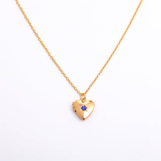 Gold heart-shaped necklace with a blue gemstone on a white background