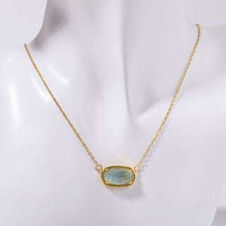 Gold necklace with a green gemstone pendant on a mannequin.