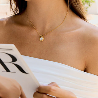 Woman wearing a gold necklace with a heart pendant, holding a magazine.