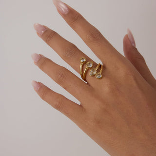 Hand wearing a gold ring with gemstones on a plain background