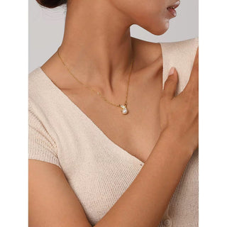 Woman wearing a delicate gold necklace with a small pendant against a neutral background