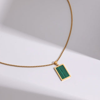 Gold necklace with a green pendant on a light gray background