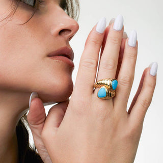 Woman wearing a gold ring with turquoise stones on a neutral background