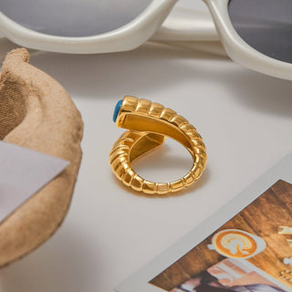 Gold ring with a blue gemstone on a surface with sunglasses and a magazine.