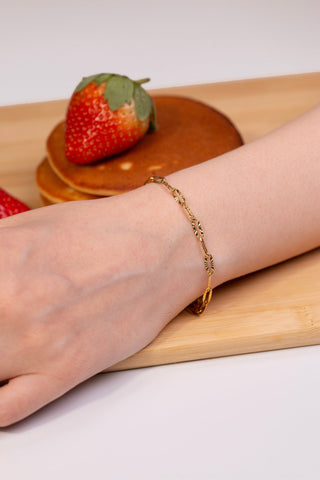 Gold bracelet on a wrist with strawberries and a wooden coaster in the background