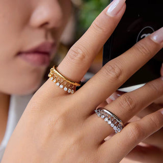 Close-up of a hand wearing two rings, one gold and one silver, with a blurred background.