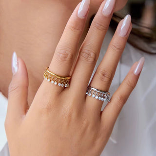 Hand wearing two rings with pearl and gemstone details on a neutral background