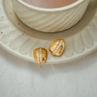 Gold earrings with gemstones on a ceramic plate with a cup of tea.