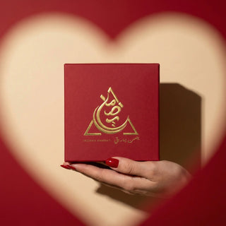 Red box with gold emblem held by a hand against a heart-shaped background