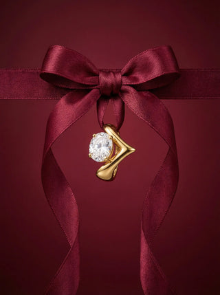 Gold earring with a diamond on a red satin ribbon against a red background