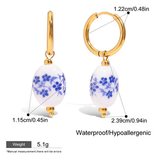 Gold hoop earrings with white beads featuring blue floral patterns, showing measurements and product details.