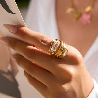 Close-up of a hand wearing a gold ring with a large gemstone, holding a white card.