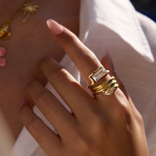 Hand wearing gold rings with clear gemstones against a blurred background