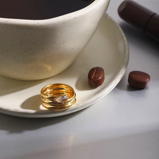 Gold ring on a white plate with a cup of coffee and coffee beans.