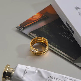 Gold ring with a diamond on a surface with a book and tube of cream.