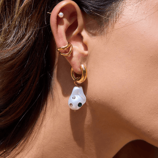 Close-up of an ear wearing gold hoop earrings with a pearl drop earring.