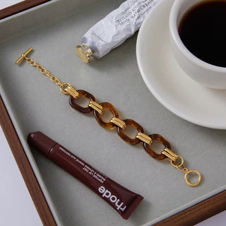 Bracelet with tortoiseshell and gold links on a tray with coffee and skincare products.