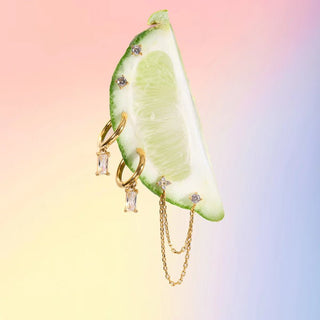 Gold jewelry with gemstones on a sliced lime against a gradient background