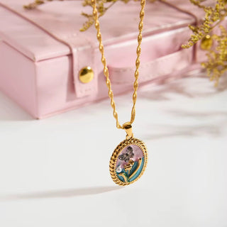 Gold necklace with a floral pendant on a light pink background
