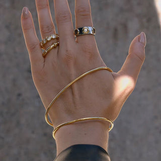 Hand wearing multiple gold rings and a bracelet against a neutral background