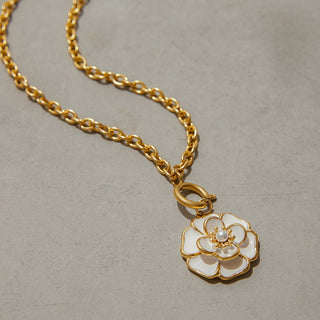 Gold necklace with a white floral pendant on a neutral background