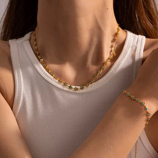 Gold necklace and bracelet on a person wearing a white tank top.
