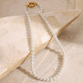 Pearl necklace with a gold clasp on a beige stone surface