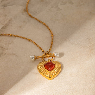 Gold necklace with a heart-shaped pendant featuring a red stone on a beige background