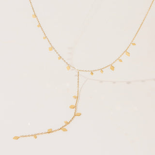 Gold necklace with leaf-shaped pendants on a light beige background