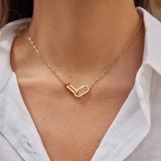 Gold necklace with a unique clasp worn by a person against a neutral background