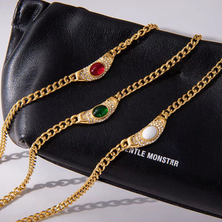 Gold chain bracelets with gemstones on a black clutch with 'GENTLE MONSTER' branding.