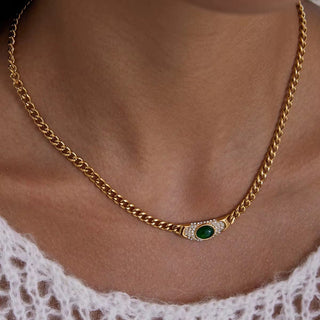 Gold chain necklace with a green gemstone and diamonds on a person wearing a white lace garment.