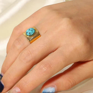 Hand wearing a gold ring with a turquoise stone on a neutral background