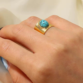 Gold ring with a turquoise stone on a person's finger against a neutral background