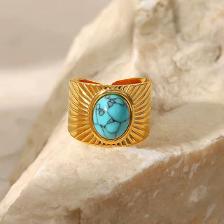 Gold ring with turquoise stone on a beige stone background