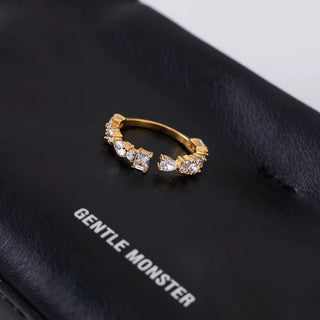 Gold hoop earring with crystals on a black surface with 'Gentle Monster' branding.