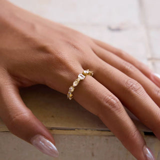Close-up of a hand wearing a gold ring with diamonds on a neutral background