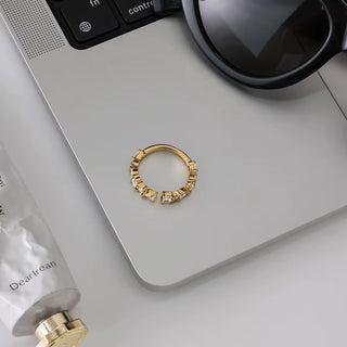Gold hoop earring on a light gray surface with a tube of cream and sunglasses.