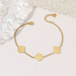 Gold bracelet with clover-shaped charms on a textured white surface
