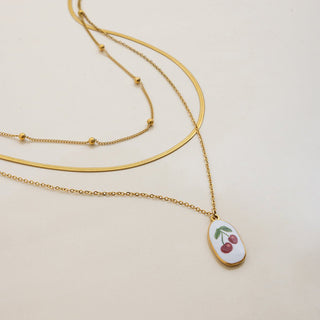 Gold necklaces with a cherry pendant on a beige background