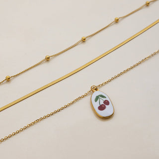 Gold necklace with a cherry pendant on a beige background