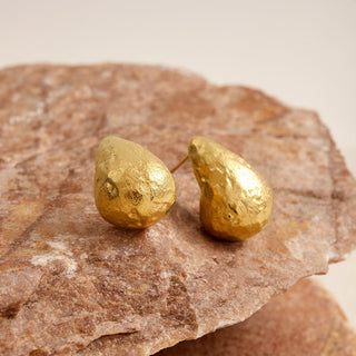 Gold teardrop-shaped earrings on a stone surface