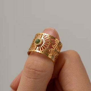Gold ring with a green gemstone on a finger against a gray background