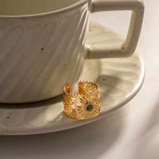 Gold ring with green gemstone on a white ceramic saucer with a cup in the background