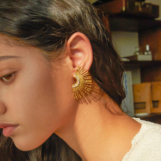 Close-up of a person wearing a gold earring with a blurred background