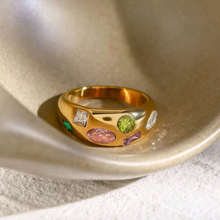 Gold ring with colorful gemstones on a textured surface