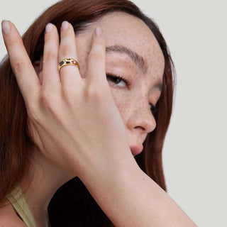 Woman with freckles on her face wearing a gold ring, against a plain background
