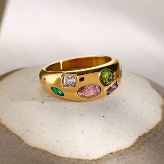 Gold ring with colorful gemstones on a textured surface